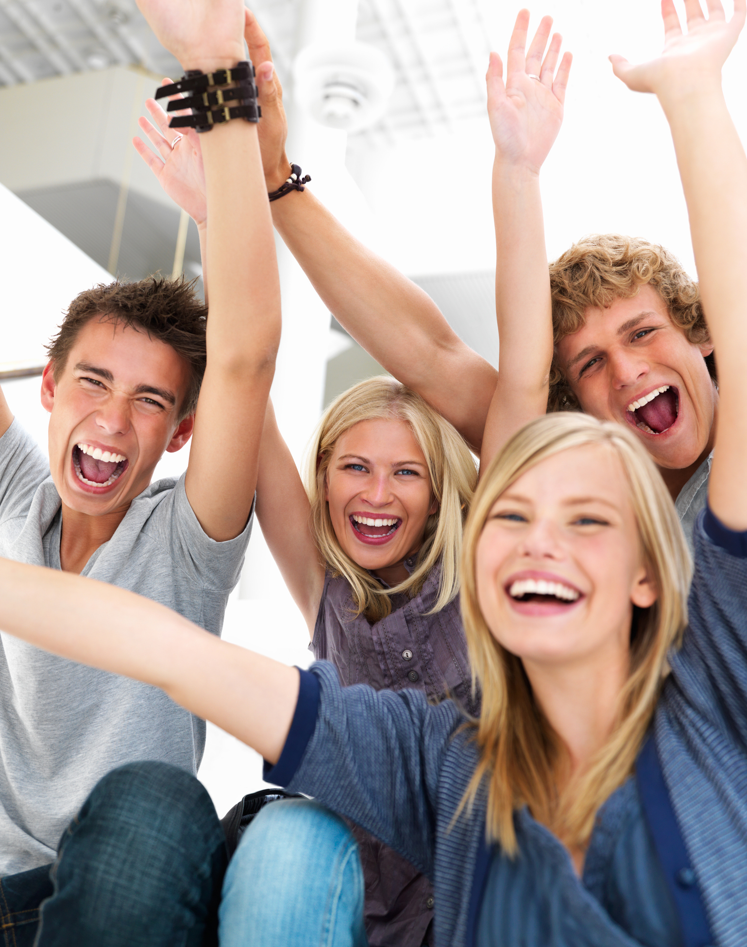 Excited teenage boys and girls shouting together with arms raised